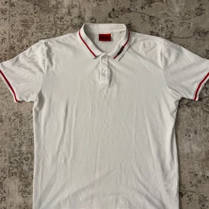 Hugo boss piké - Vit Hugo Boss piké med logga på kragen. Den är knappt använd och är i väldigt bra skick, storlek L och nypris är 1000kr.