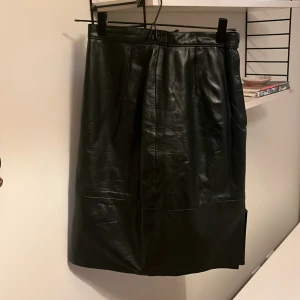 Läderkjol  - Mörkgrön vintage läderkjol köpt second hand. Slit och dragkedja samt knapp på vänstersida. Bra skick. ”Pencilskirt” passform. Märke: Genuine leather 🫶