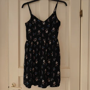 Kort blommig sommarklänning  - Sommarklänning med blommigt mönster  Justerbara axelband  Stretchigt material i ryggen (se bild)  Använd fåtal gånger så i fint skick  Slutar strax ovanför knäna på mig (173 cm som referens)