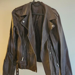 Skinnjacka - Snygg brun skinnjacka. Ej äkta läder. Har fickor och dragkedja. Bra skick.