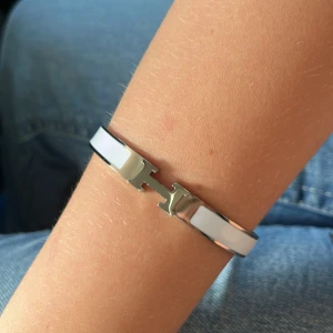 Vitt armband med silverdetaljer - Ett elegant vitt armband med silverdetaljer. Armbandet har en stilren design och är perfekt för både vardag och fest.