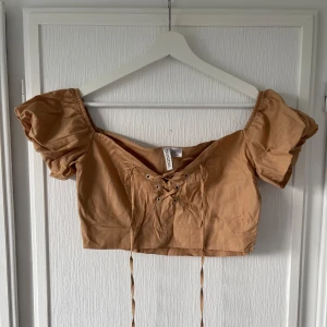 Ljusbrun topp - Snygg ljusbrun topp med lite puffiga ärmar som aldrig är använd. Knytdetalj där fram. Icke stretch. I mycket bra skick. 
