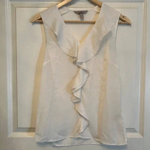 Blus-linne H&M - Vitt linne i blusmaterial med volanger vid halsen som sedan går dubbelt hela vägen ner. Varsamt använd några gånger. 100 % polyester.   Pris kan diskuteras. Köparen står för frakt. Hör gärna av er för fler bilder eller frågor. 