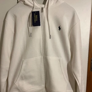 Ralph lauren polo  -  "Klassisk Ralph Lauren zip-up Hoodie i stilren vit färg. Perfekt för en avslappnad och stilfull look. Bekväm passform och hög kvalitet. Ett mångsidigt plagg som passar både till vardags och tillfällen när du vill ha en avslappnad elegans."