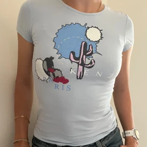 Ljusblå tight T-shirt med tryck - Ljusblå tight T-shirt med kaktus motiv i storlek 12 år/XS från Kenzo.  T-Shirten är i gott skick!