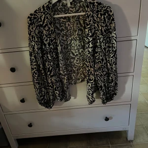 Svartvit mönstrad jacka - En svartvit mönstrad jacka med långärmad design. Jackan har ett öppet framstycke utan knappar eller dragkedja.