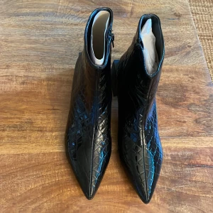 Svarta stövletter från NLY Shoes - Ett par svarta stövletter från NLY Shoes med krokodilpräglat mönster. Skorna har spetsig tå och en klack.