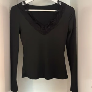 Svart topp - En svart v-ringad topp med spets i v-ringingen. Aldrig använd alltså i nyskick utan defekter.