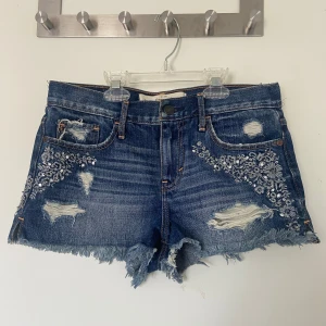 Abercrombie & Fitch lågmidjade jeans, stl 25 - Lågmidjade jeansshorts med paljett detaljer i fint skick!  Frakt tillkommer, plagg som köps kan samfraktas!