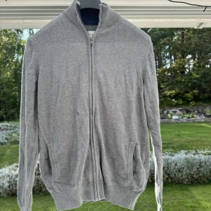 Tunnare kofta - Grå tunn kofta med dragkedja samt fickor, innerkragen är marin blå. Väldigt fint skick då den används bra. Fint stickad och mjuk i materialet. Storlek S men passar även M då materialet är stretchigt. 