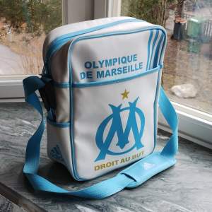 Grym Olympique de Marseille messenger bag från Adidas. Köpt på plats i Marseille i supportershoppen för massa år sedan. Knappt använd men finns ändå slitningar som bild 3 t.ex.