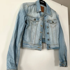 Jeans jacka - Oversized jeansjacka med vintage look. Jackan är vit och har knäppning fram. Den har nedhasad axel, bröstfickor med lock, krage, reglerbar slejf med knapp i sidorna och lång ärm med knapp och manschett.