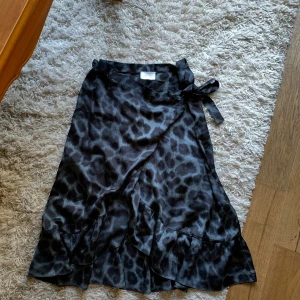 Svart leopardmönstrad omlottkjol från Neo Noir - Säljer en superfin svart leopardmönstrad omlottkjol från Neo Noir. Kjolen är i storlek L men går att knyta till så att den passar fler storlekar. Den har en volangdetalj och knytning i midjan 🖤