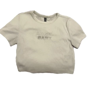Croptop - En söt vit ribbad croptop med silver glittrig text: ANGEL BABY. Inga defekter men lite nopprig (sänkt pris) som man ser på närbilden av trycket!!❤️ Ställ gärna frågor❤️✨