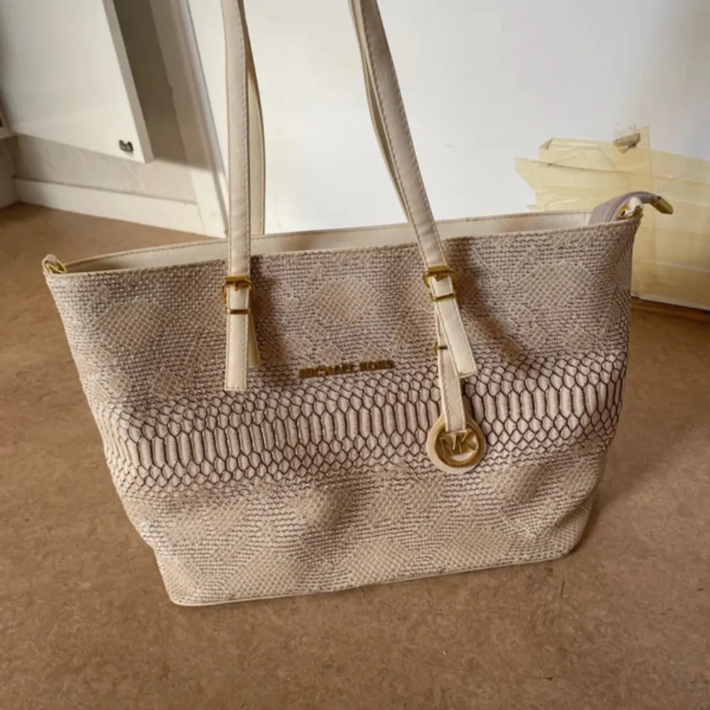 En elegant beige handväska från Michael Kors med ett ormskinnsmönster. Väskan har två långa handtag och en avtagbar axelrem. Den har en dragkedja och flera innerfickor för förvaring. kan ej garantera äktheten!. Laukut & Käsilaukut.