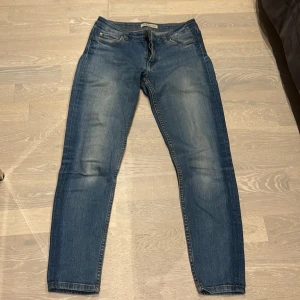 Blå jeansbyxor - Säljer ett par snygga blå jeansbyxor. De har en klassisk femficksdesign och en dragkedja med knapp framtill. Byxorna har en lätt slitning på framsidan och baksidan vilket ger dem en cool och avslappnad look. Perfekta för vardagsbruk!