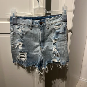 Ljusa jeansshorts från Fashion Nova - Ljusa jeansshorts från Fashion Nova med slitna detaljer och fransig nederkant. Shortsen har en knapp och dragkedja framtill samt fem fickor.