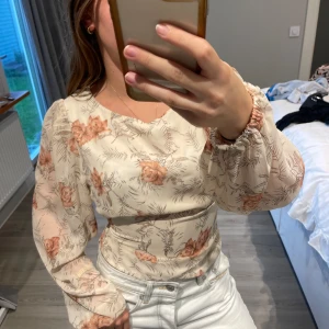 Blommig blus från Rut&Circle - Säljer en superfin blommig blus från Rut&Circle i storlek M. Blusen är beige med ett vackert blommönster i rosa och har långa ärmar med resår vid ärmsluten. Den har en knytning i ryggen som ger en snygg detalj. Perfekt för både vardag och fest!