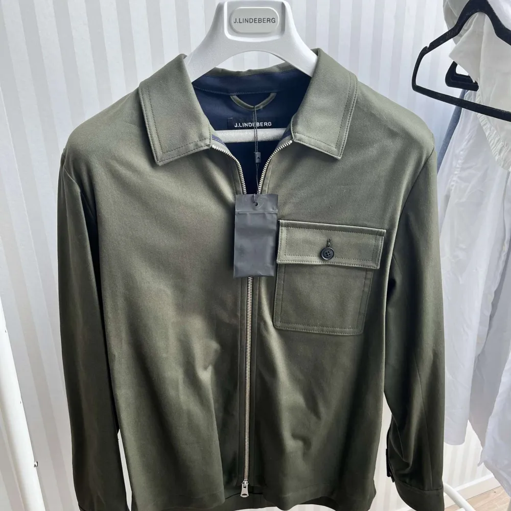 Säljer en snygg olivgrön overshirt från J.Lindeberg. Den har en dragkedja framtill och en bröstficka med knapp. Perfekt för vår och höst, och kan bäras både som en jacka eller som en skjorta. Materialet känns mjukt och bekvämt, och passformen är normal. Perfekt för en stilren och avslappnad look!. Jackor.