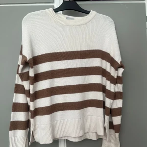 Randig stickad tröja - Säljer en superfin randig stickad tröja i vitt och brunt. Den har en normal passform och är långärmad med ribbade muddar vid ärmslut och nederkant. Perfekt för höst och vinter! 🧡