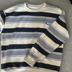 Randig tröja från Peace - Säljer en snygg randig tröja från Peace i storlek M. Tröjan har ett coolt mönster med svarta, gråa, vita och blåa ränder. Den är långärmad och har en normal passform. Perfekt för höst och vår💕