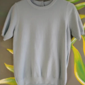 Ljusblå stickad T-shirt - Supersöt ljusblå t-shirt med tre guldknappar i bak, aldrig använd💕💕