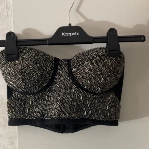 Bandå Topp - En bandå topp med nitar och pärlor på av silver. Lite edgy. Har en dragkedja på baksidan. Bröst kupan är C/D.