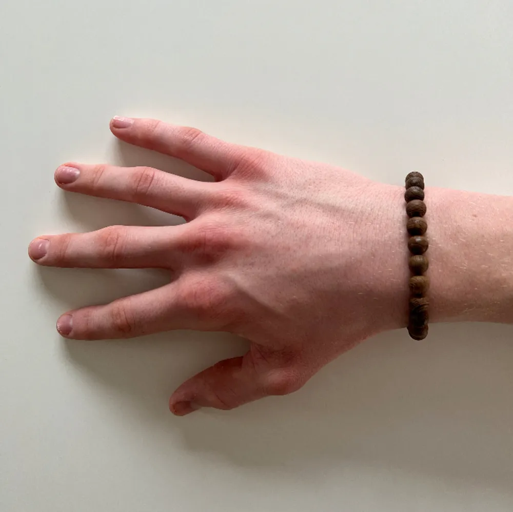 Pärlarmband med bruna träpärlor och en silvrig mellandel (livets träd). Demeter är ett stilrent armband som passar såväl till vardags som till festligare ögonblick. Armbandet har en omkrets på cirka 19 cm.. Accessoarer.