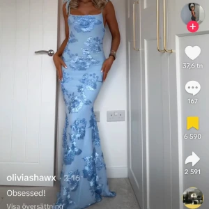 Ljusblå långklänning med blommor - Supersnygg ljusblå långklänning med blommigt mönster och smala axelband som knyts på axlarna. Klänningen har figurnära passform och en elegant, feminin siluett. Perfekt för dig som vill sticka ut med en romantisk vibe och älskar detaljer!