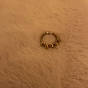Guldfärgad ring med nitar - Cool ring i guldfärg med fyra spetsiga nitar runt om. Perfekt accessoar för dig som gillar edgy och unik stil. Ringen har en rund form och är enkel att matcha med andra smycken.