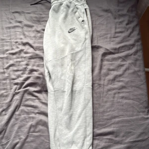 Grå mjukisbyxor från Nike /spodnie od nike - Snygga grå mjukisbyxor från Nike med klassisk logga på benet. Byxorna har resår i midjan med snörning och är tillverkade i mjukt bomullsmaterial. Perfekta för chill eller träning, med en relaxed passform och praktiska fickor. Den har några skador som du kan se i bilderna 