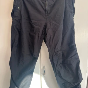 Svarta byxor från Urban Outfitters - Svarta cargopants från Urban Outfitters i storlek XL. Byxorna har dragkedja framtill, snörning vid benslut och flera fickor. Tillverkade i bomullsmix, loose fit och perfekt för en chill streetwear-look.