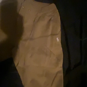 Beiga chinos från Polo Ralph Lauren - Snygga beiga chinos från Polo Ralph Lauren med klassisk passform och broderad vit logga på fickan. Byxorna har diskreta knappar i midjan och är perfekta för en clean och stilren look. Tröja finns till