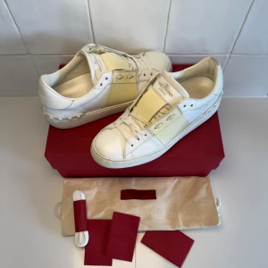 Valentino skor  - Snygga Valentino Garavani Open sneakers i vitt skinn med ljusgul detalj över mitten. Klassisk rund tå, snörning och ikoniska nitar baktill. Dustbag, snören, kort medföljer vid köp!! Bara att höra av sig till oss vid minsta fundering😁