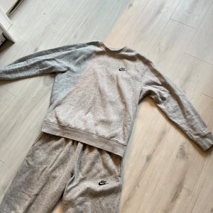 Nike set - Ett klassisk grått set från Nike med svart broderad logga på bröstet och byxorna. Tröjan har rund halsringning och långa ärmar. Tillverkad i mjuk bomullsblandning som är perfekt för chill eller träning.