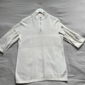 Vit stickad polotröja med half zip - Snygg vit stickad polotröja med halv dragkedja framtill och strukturstickade detaljer på bröstet, ärmarna och nederkanten. Tröjan var en ribbad krage som ger en clean och modern look. Perfekt för dig som gillar stilrena plagg.