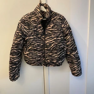 Trendig croppad pufferjacka i zebramönster i beige och svart ! - Supercool pufferjacka i beige och svart zebramönster – perfekt för dig som vill sticka ut med en unik och trendig look. Jackan är croppad med hög krage, dragkedja framtill och två stora fickor.                       