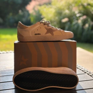 Golden goose skor - Snygga beige sneakers från Golden goose med klassisk låg profil, rund tå och platt sula. Skorna har en ikonisk stjärndetalj i mocka på sidan, matchande beige snörning och GGDB-logga. Ovandelen är i skinn och detaljer i mocka ger en stilren look. Om ni har några frågor så är de bara att höra av er!😁