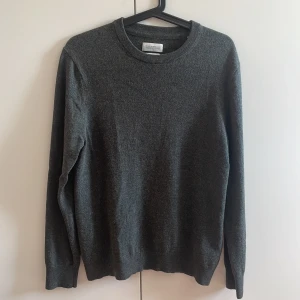 Mörkgrå merinoulltröja These Glory Days - Snygg mörkgrå stickad tröja från These Glory Days i mjuk superior merinoull. Rund halsringning och långa ärmar, perfekt för dig som gillar stilrena och klassiska plagg med skön passform. Enkel att matcha med jeans eller chinos.