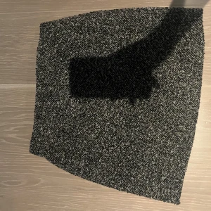 Svartgrå kortkjol  - Snygg svartgrå kortkjol med diskret fiskbensmönster. Kjolen har en rak passform och är tillverkad i en mjuk ullblandning som passar perfekt till kyligare dagar. Enkel att matcha med både stickade tröjor och boots.