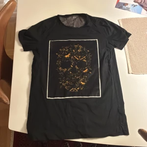Svart t-shirt Limitato med döskalletryck - Svart t-shirt från Limitato med korta ärmar och ett stort tryck framtill som föreställer en döskalle gjord av fjärilar i orange och gult. Skön passform och tillverkad i mjuk bomull. Tshirten är i bra skick 8/10 och har inga defekter. Riktigt snygg och fräsch tröja.Storlek Xs men passar även folk som har storlek S