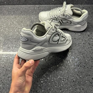 Gråa b30 storlek 42 - Dior B30 – Grå Säljer ett par gråa Dior B30 sneakers. Riktigt snygga och sköna skor med modern design som passar till det mesta. 	•	Storlek: 42 	•	Nypris: ca 10,000kr  Perfekta för dig som vill ha ett par lyxiga sneakers som sticker ut men ändå är enkla att bära till vardags. (Skickas utan box)