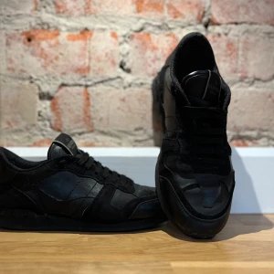 Valentino Garavani Rockrunner svart - Svarta Valentino Garavani Rockrunner sneakers i mix av skinn och mocka med tonade paneler och klassisk snörning. Snygg, sportig siluett med diskret camo-detalj och logga på plösen. Perfekta för dig som gillar exklusiva och stilrena sneakers.