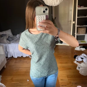 Grön stickad topp från Jacqueline de Yong - Snygg grön stickad topp från Jacqueline de Yong med korta ärmar och ett coolt hålmönster i hela tyget. Toppen har rund halsringning och är i en mjuk, stickad kvalitet som känns luftig och fräsch. Perfekt att styla med jeans eller kjol för en chill look. Lite oversized o stor på mig som har strl XS/S men funkar!