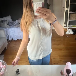 Vit ärmlös blus från H&M - Säljer en stilren vit blus från H&M med ärmlös design och lätt v-ringning framtill. Toppen har en mjuk och slät känsla, perfekt till jeans eller kjol. Enkel och clean look som passar till många olika outfits. Storleken står inte o jag kommer inte ihåg men den passar mig lite oversized som XS. Passar även S samt M!!!
