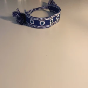 Blå tygarmband med ögonmönster som är hemmagjort!!! - Snyggt blått tygarmband med broderade ögonmönster i vitt och ljusblått. Jag har gjort det ensam hemma!!! Med lite hjälp från min mamma… Säljer ett för 130kr och två för 180kr!! Skriv för mer frågor!🙂