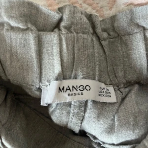 Grå linnebyxor från Mango XS - Snygga grå linnebyxor från Mango Basics i storlek XS. Byxorna har raka ben, elastisk midja med knytband och bakfickor. Perfekta för en chill och stilren look under varmare dagar. Liten bristning baktill men inget som syns så mycket och går att fixa.