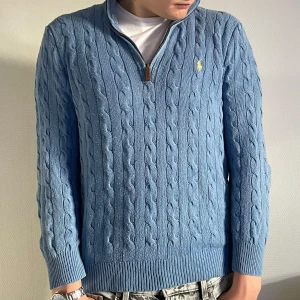 Blå Kabelstickad Half-Zip från Ralph Lauren - Kabelstickad blå tröja från Polo Ralph Lauren med halv dragkedja och klassisk gul logga på bröstet. Tröjan har hög krage, ribbade muddar och är långärmad. Perfekt för lager-på-lager och chill stil. Endast använd fåtal gånger. Nypris 2695kr!