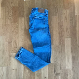 Jack and Jones Jeans - Säljer ett par blå skinny jeans från Liam i storlek 31/32. Jeansen har klassisk femficksdesign, normalhög midja och är tillverkade i ett stretchigt denimtyg för en tight passform. Perfekta för dig som gillar en smal siluett och enkel stil.