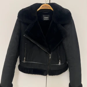 Svart pälsjacka från Pull&Bear - Säljer en superfin svart jacka från Pull&Bear i bikermodell som jag har knappt använt. Jackan har mjukt fuskpälsfoder på insidan, kragen och ärmsluten som gör den både varm och stilren. Perfekt till höst- och vinterjacka. Storlek S (passar även XS beroende på hur man vill att den sitter)